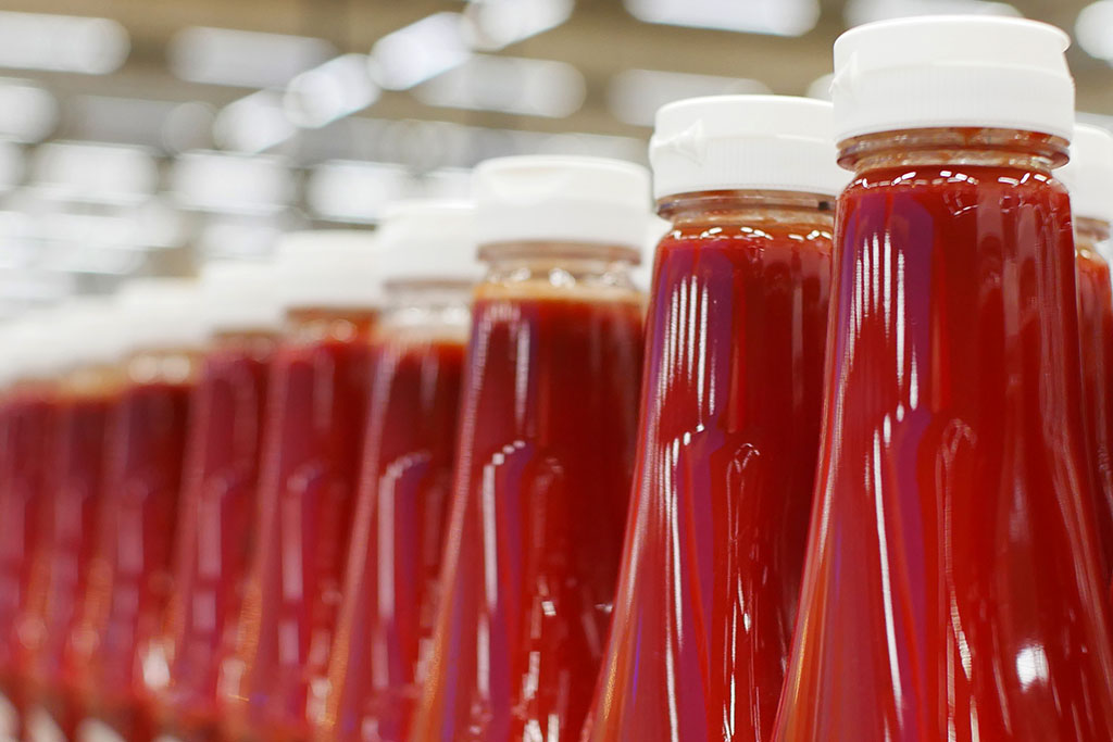 Many bottles of ketchup standing in a row in a factory